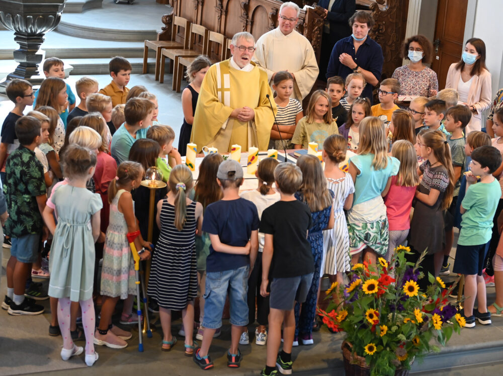 Einige Erwachsene und viele Kinder stehen bei einem Gottesdienst um den Altar.